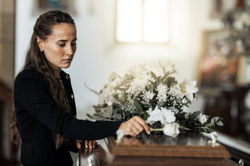 Une femme en deuil dépose une fleur sur un cercueil lors d’une cérémonie funéraire, illustrant l’aide offerte par la prestation de décès au Québec.