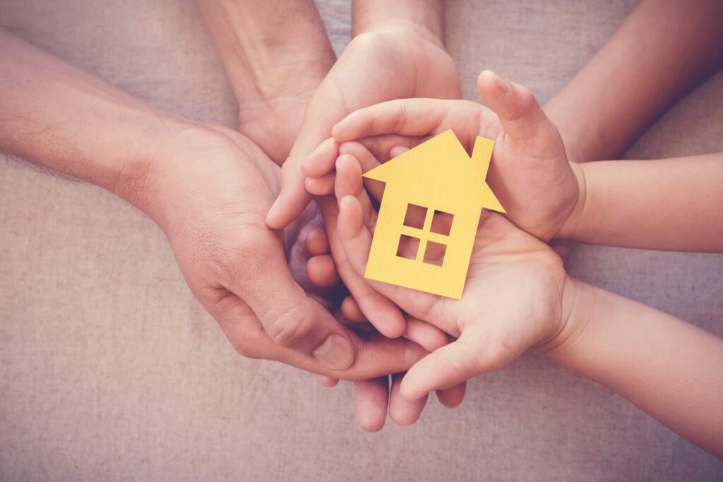 Des mains d’adultes et d’enfants tiennent une maison en papier, symbolisant le soutien familial et l’accès au logement grâce au Programme HLM au Québec.